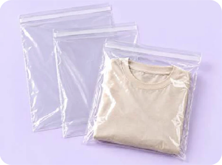 Tres bolsas transparentes con franja adhesiva en la boca; la de adelante tiene una remera beige doblada y las otras, vacías